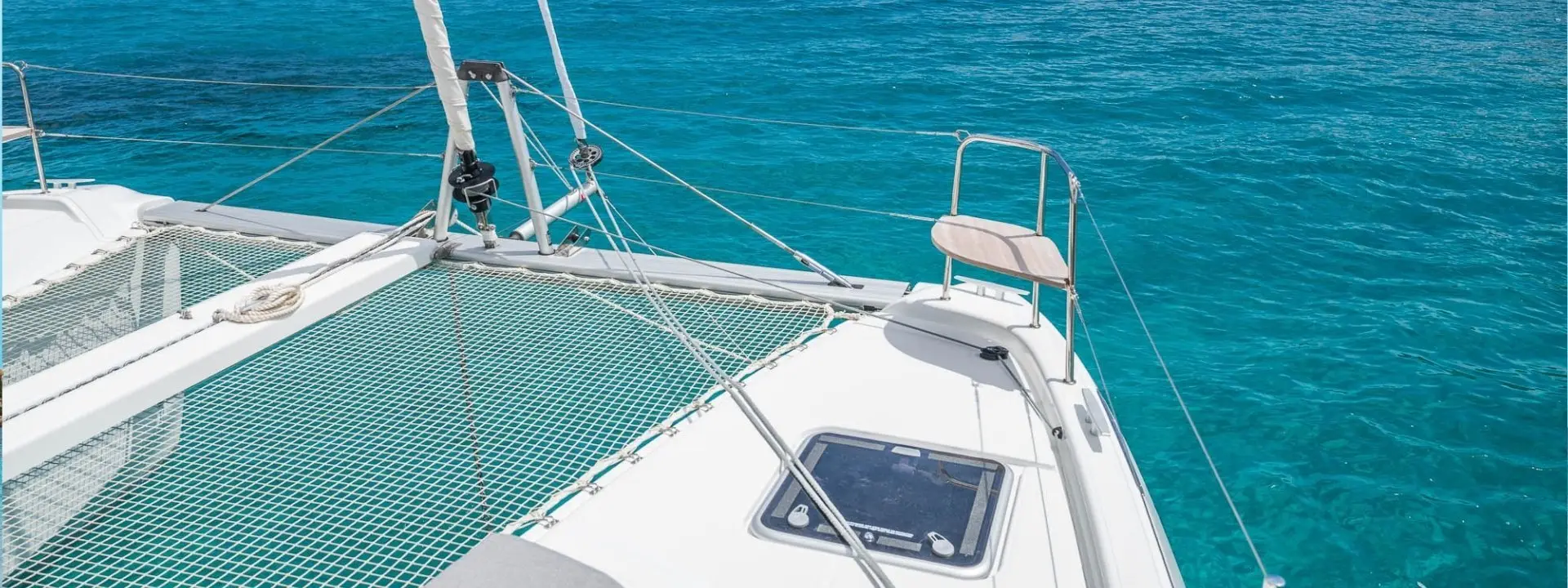 Front deck of a white Lagoon 38 catamaran with netting over the water, floating on clear, bright turquoise sea under sunny skies.
