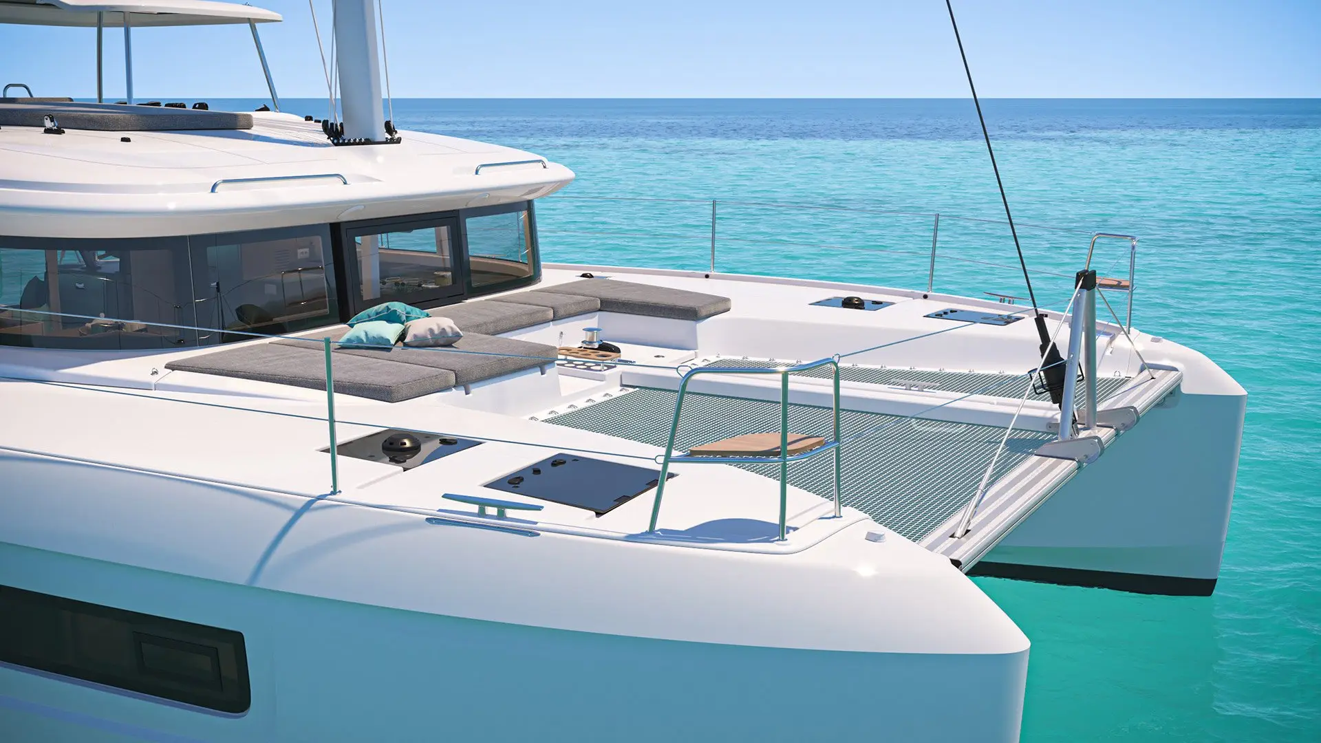 A modern white catamaran with sunbeds and lounging cushions on deck, floating on calm, turquoise water under a clear blue sky.