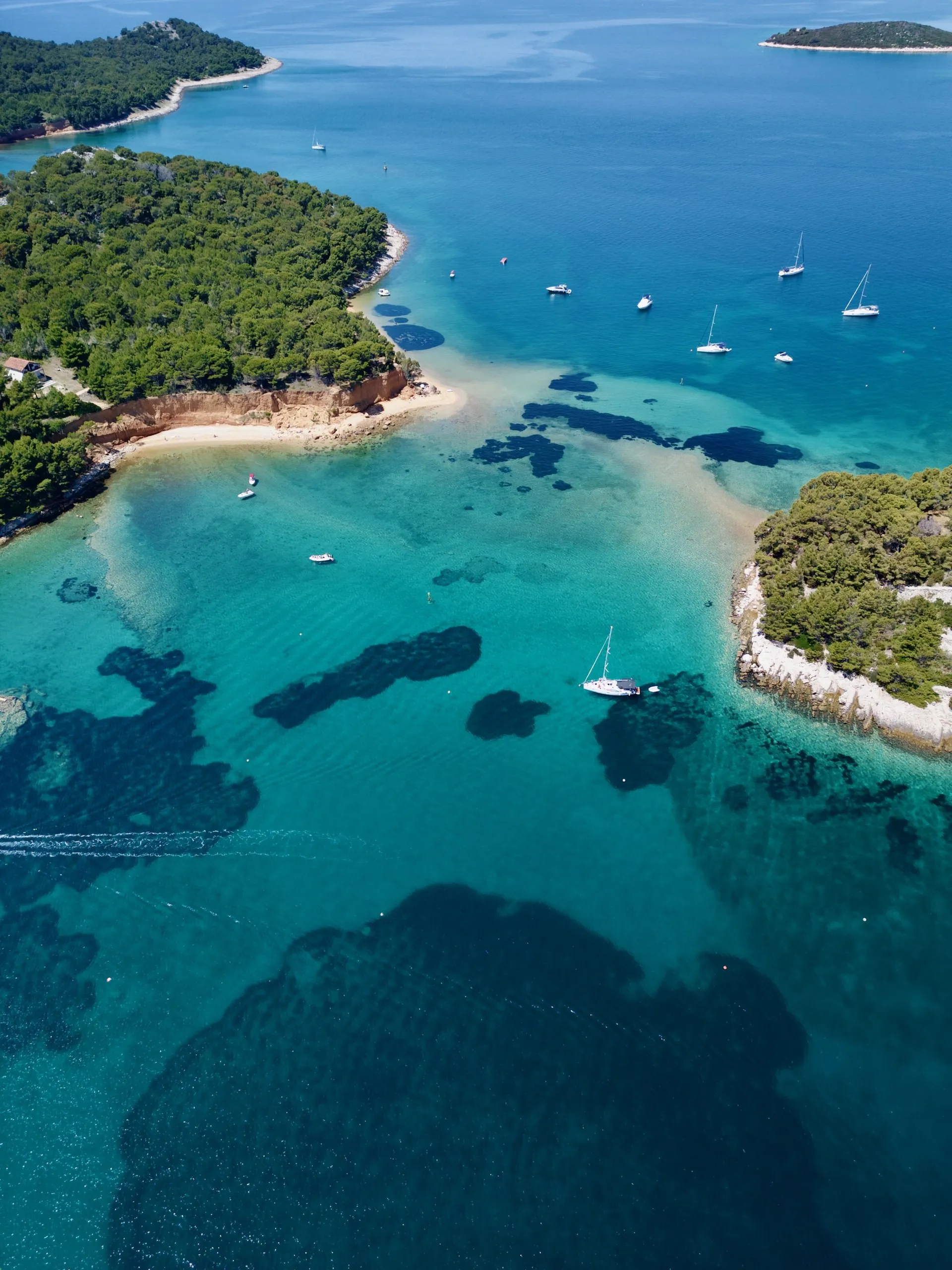 Shallow bay on Drvenik with Lagoon catamarans anchored near a green, wooded shore