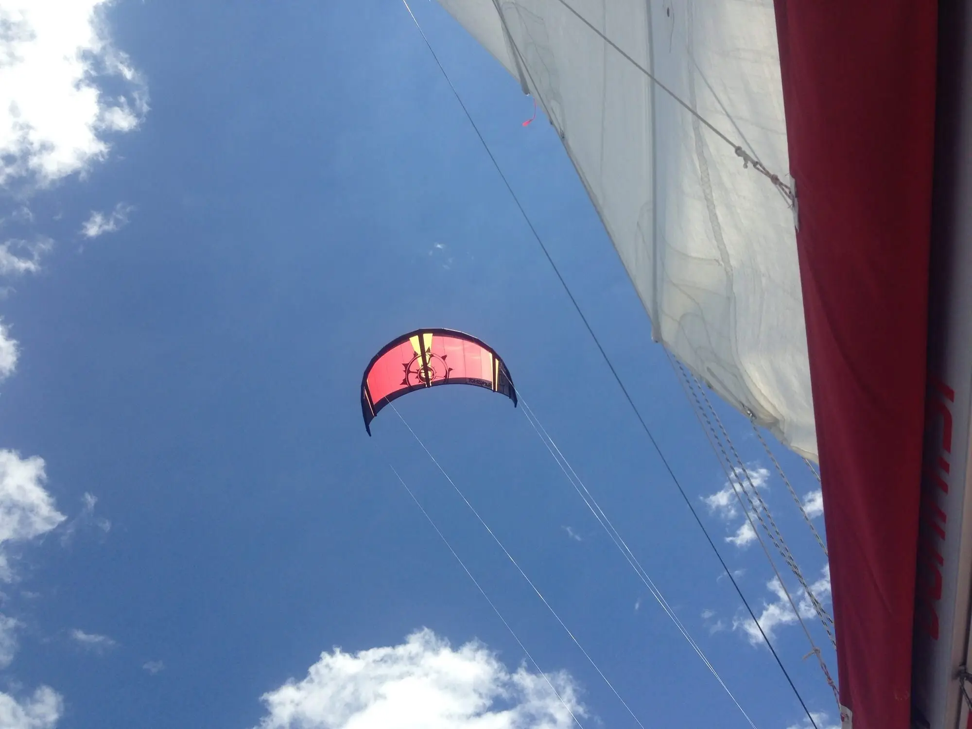 A red kite in a blue sky seen from the deck, next to the sails of the yacht.