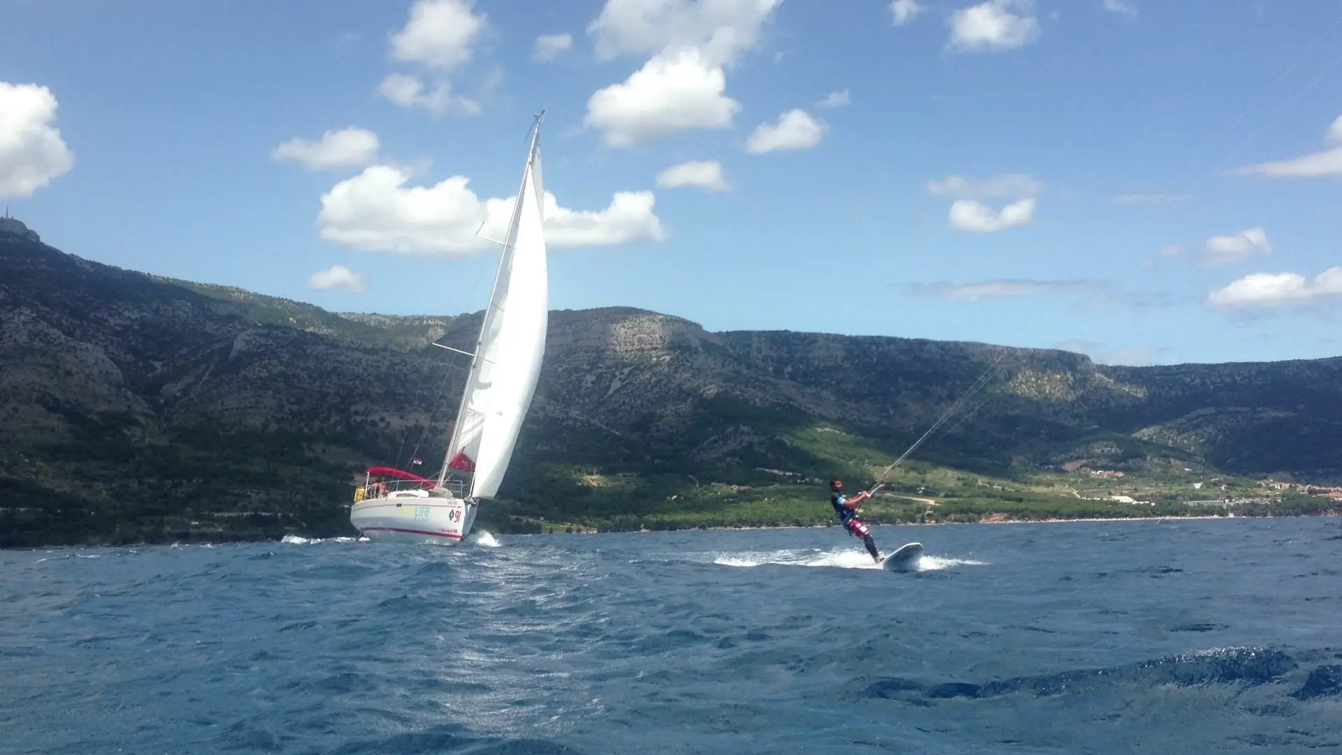 A kitesurfer and a sailing yacht in a channel between mountainous islands.