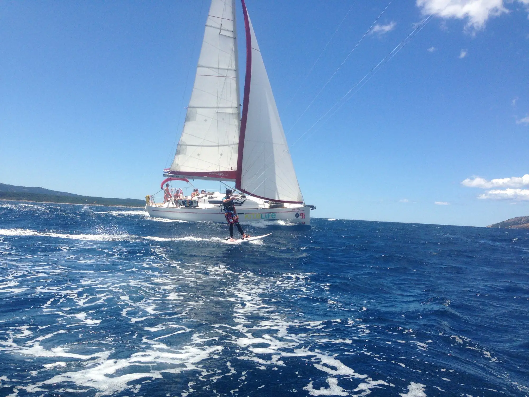 A windsurfer on blue water with a large white sailboat behind, under a sunny sky.