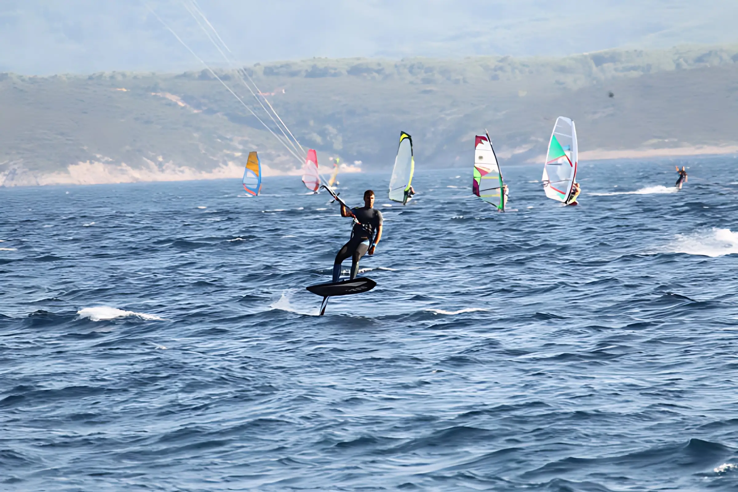 Kite foiler riding among windsurfers, green island hills behind