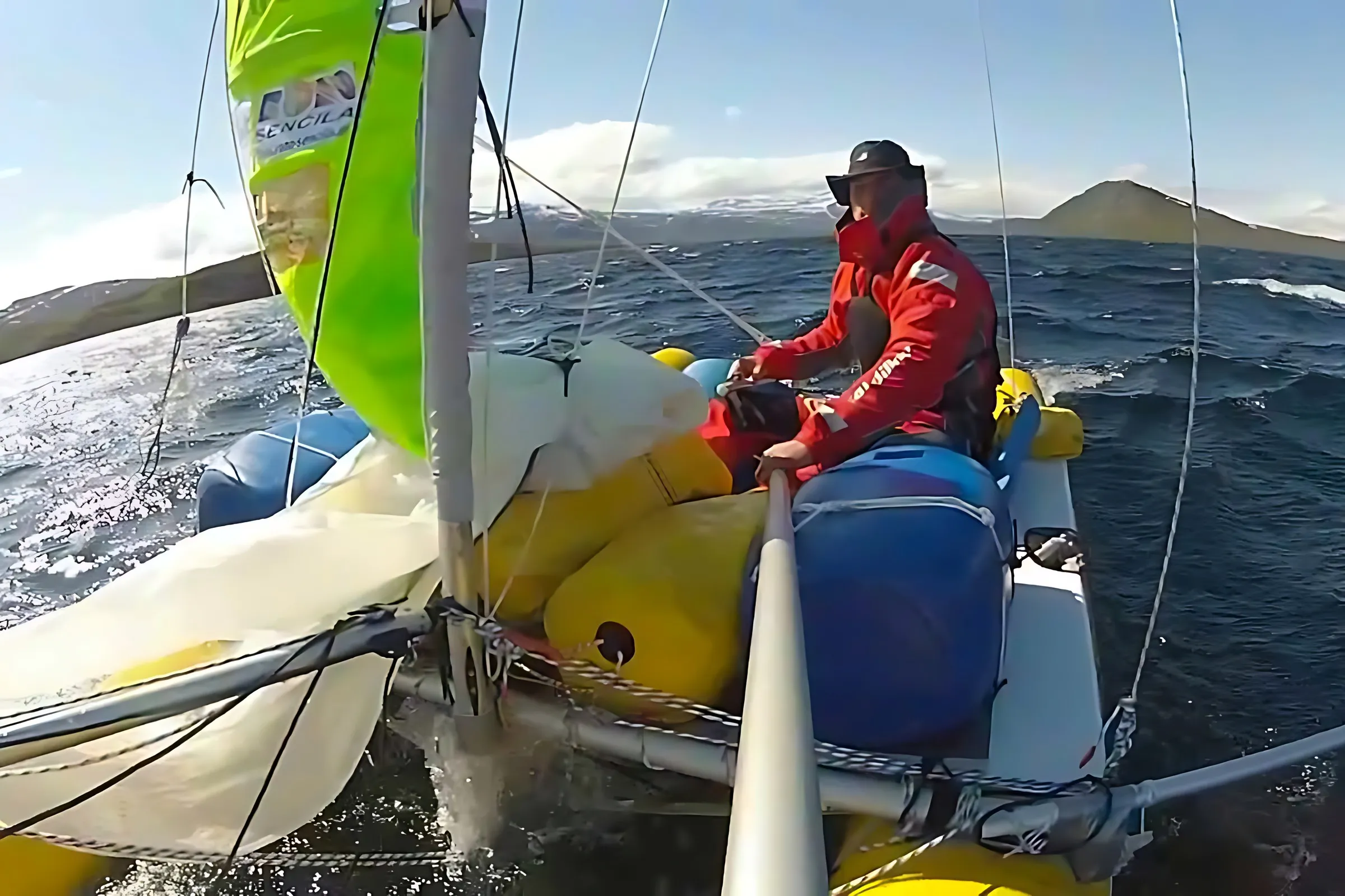 Sailor in foul-weather gear trimming on a small catamaran in fresh wind